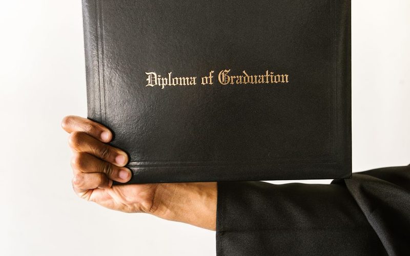 A graduate holding a diploma in a dark cover